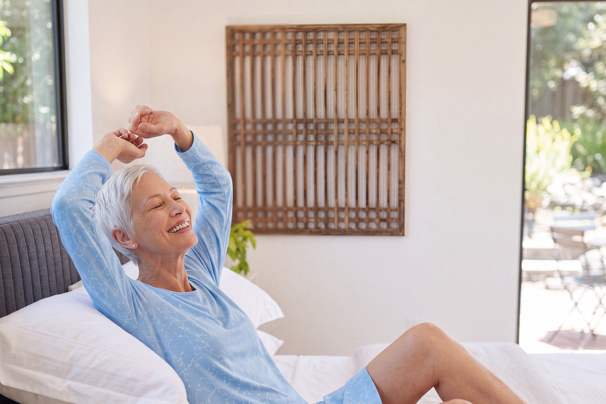 Smiling woman stretching her arms overhead in bed in a light blue print NightCool long sleeve scoop neck nightshirt
