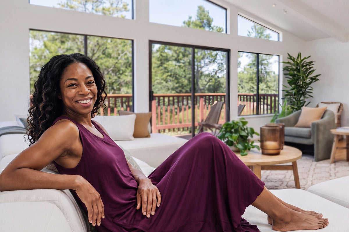 Smiling woman reclining on a white sofa in a long sleeveless NightCool tank gown in Merlot