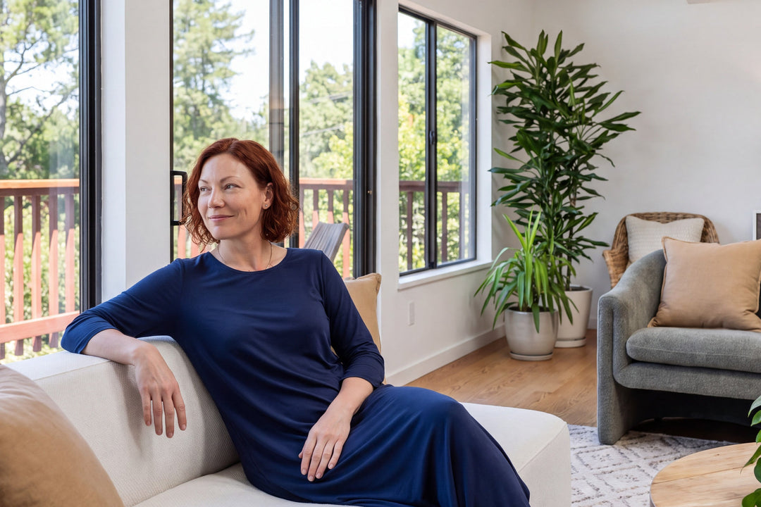 Woman resting on a sofa in a sunlit living room in a navy NightCool long scoop neck nightgown with 3/4 sleeves
