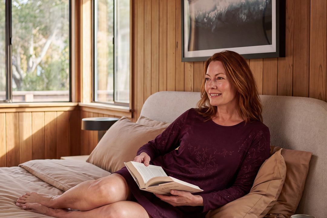 Woman reading in bed in a merlot vine print NightCool long sleeve scoop neck nightshirt