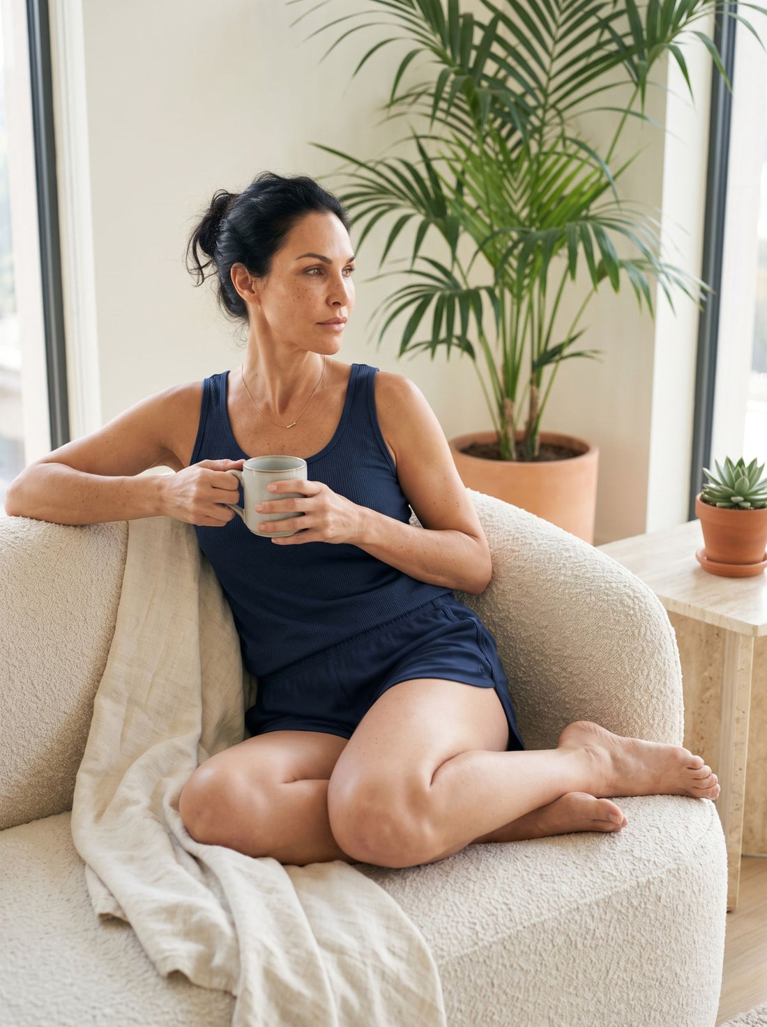 Woman relaxing on a boucle sofa in a navy NightCool tank and shorts set