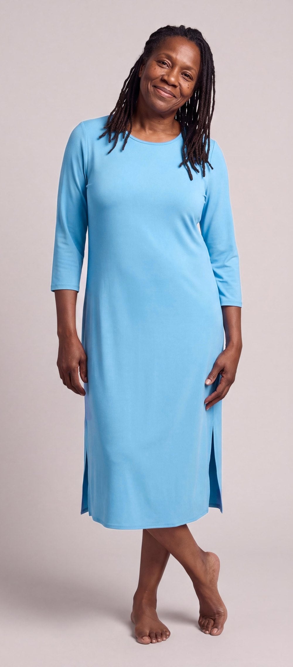 A woman in the DayBasics Long Scoop Neck Nightgown with 3/4 Sleeves in Island, smiling, ankles crossed